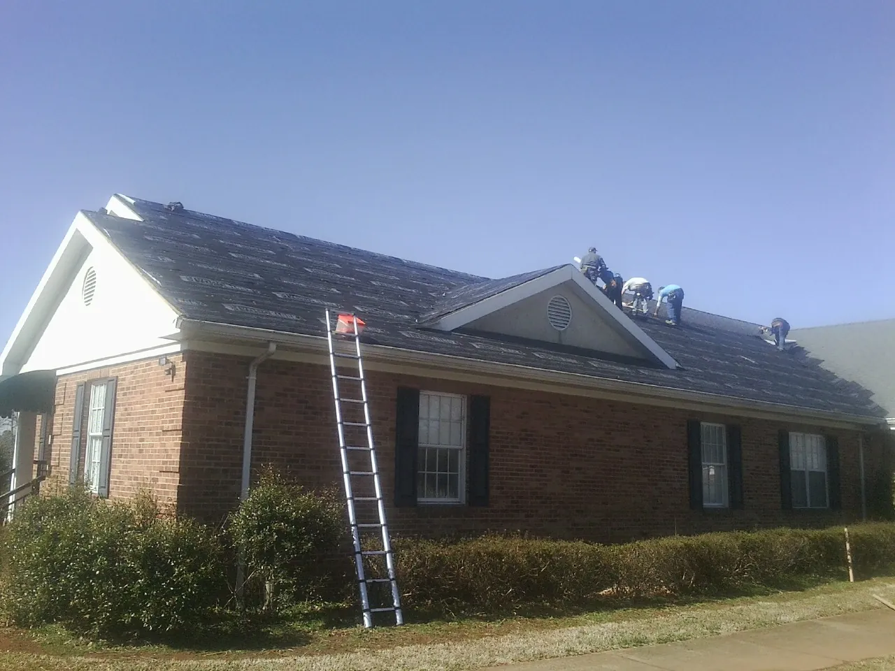 Crew tearing shingles off a brick ranch roof with a ladder set — Emergency Roof Repair work by our crew in Perkasie