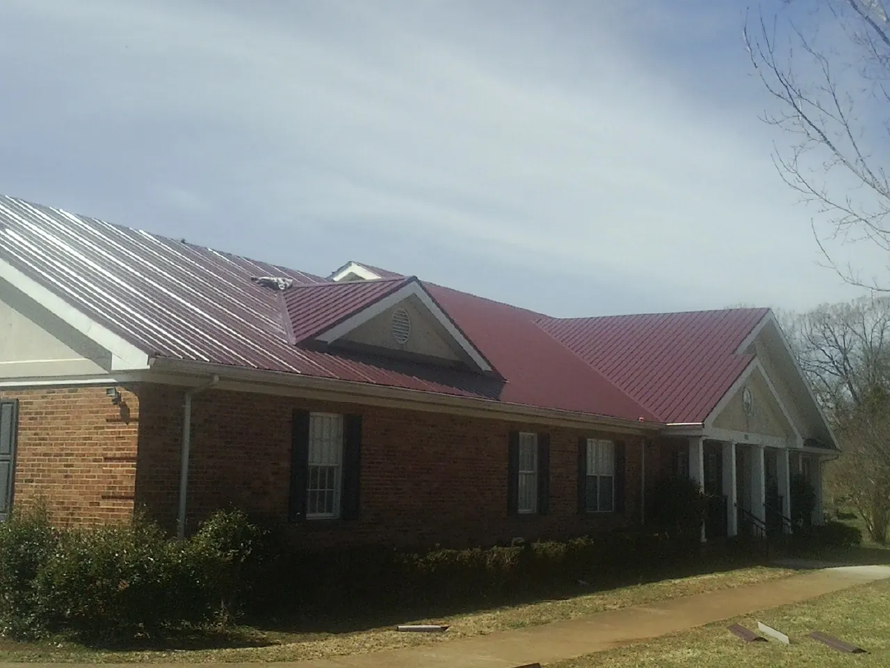 Red metal roof with gabled entries on a long brick building, from a Hail Damage Roof Repair job in Perkasie