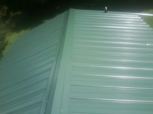 New green metal panels meeting at the ridge of a roof — Flat Roof Repair work by our crew in Perkasie