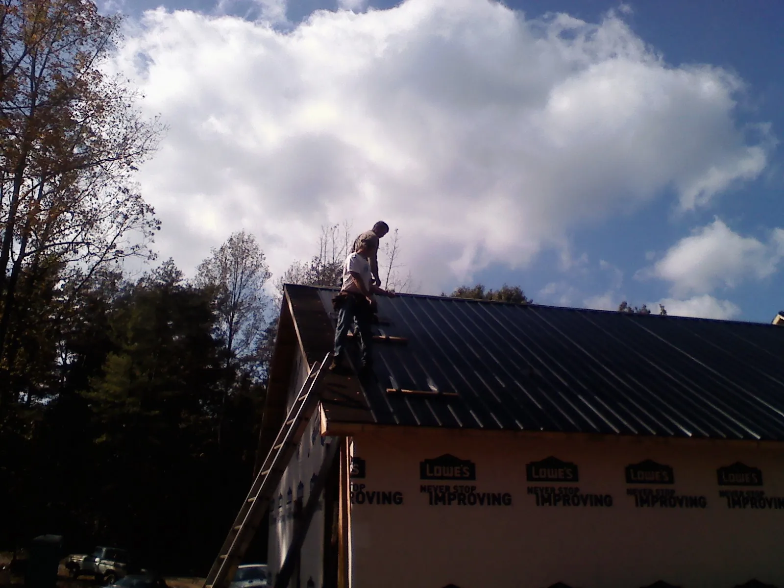 Roofer fastening dark metal panels high against a cloudy sky, from a Roof Inspection job in Perkasie