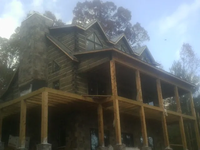 Stone chimney and dormers on a large log home with a timber porch in Perkasie