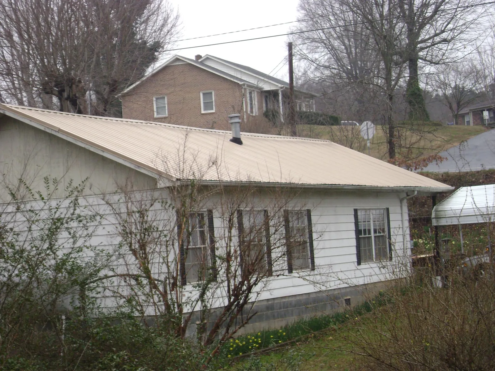 Tan metal roof on a white sided house set into a hillside — Commercial Roofing by Roofing Brothers in Perkasie